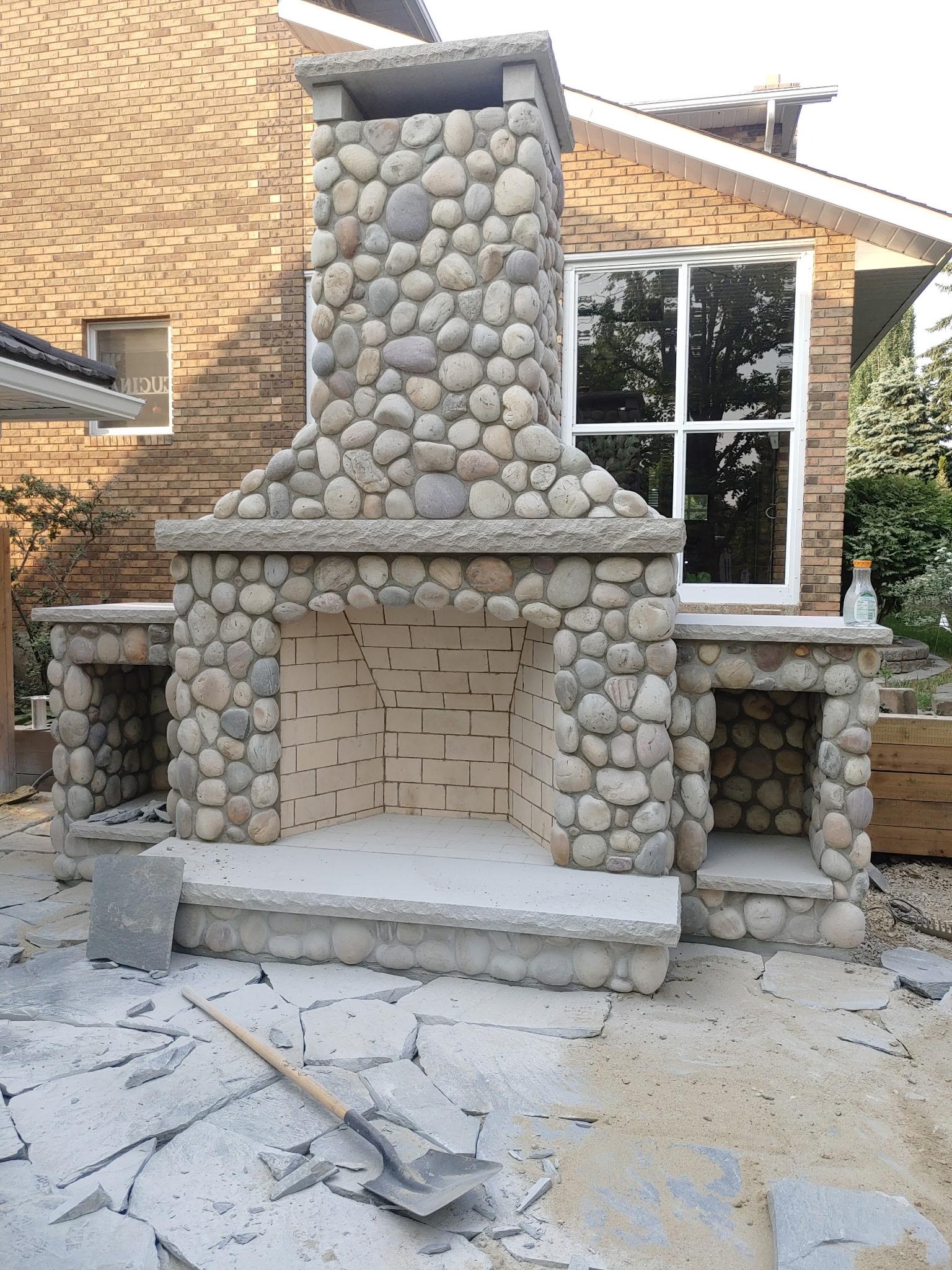 Outdoor river rock fireplace structure with arched opening on flagstone patio